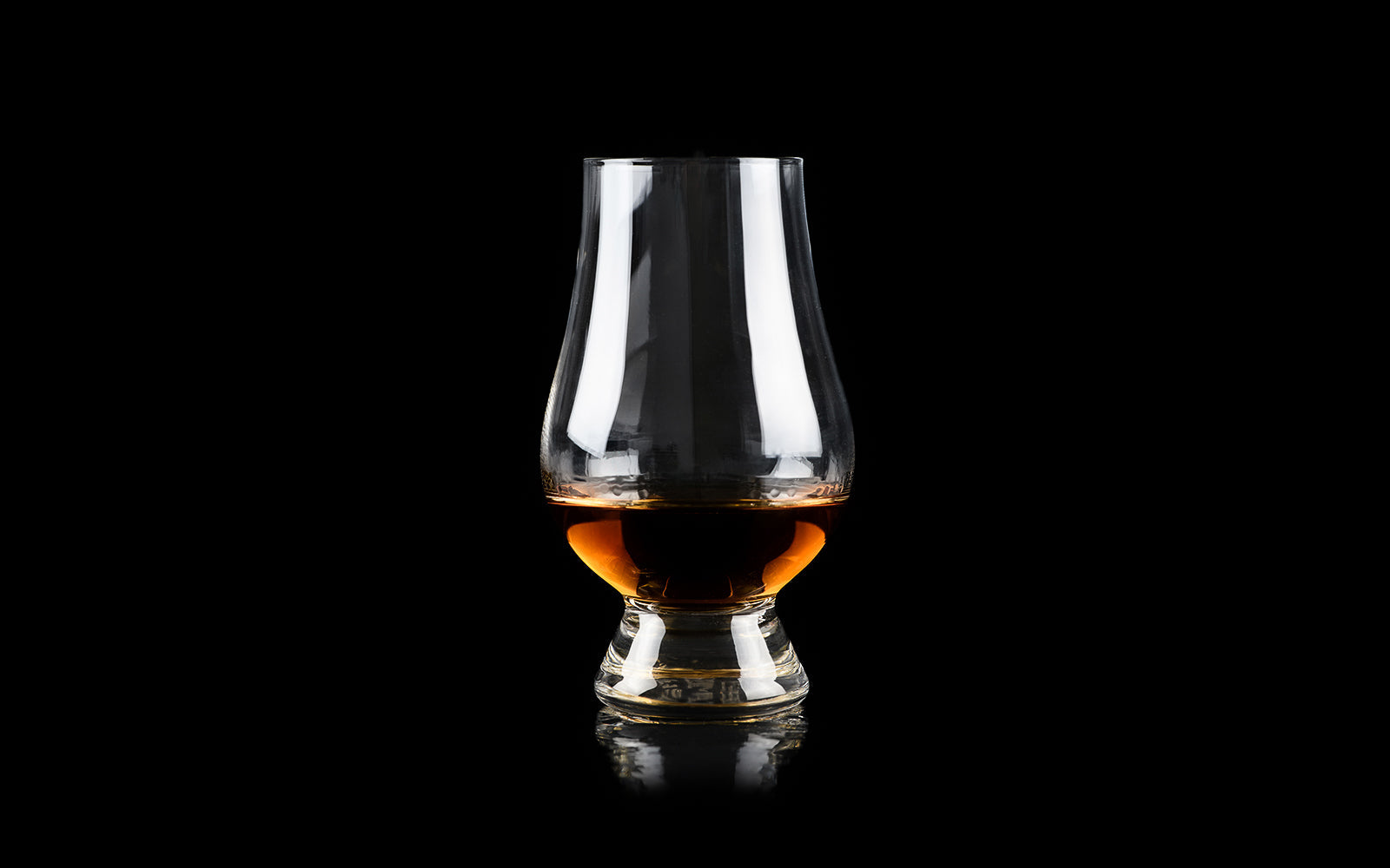 A Glencairn tulip nosing glass of amber whisky on a black background, its shape designed to concentrate aroma. Baroque Whisky Australian Single Malt.