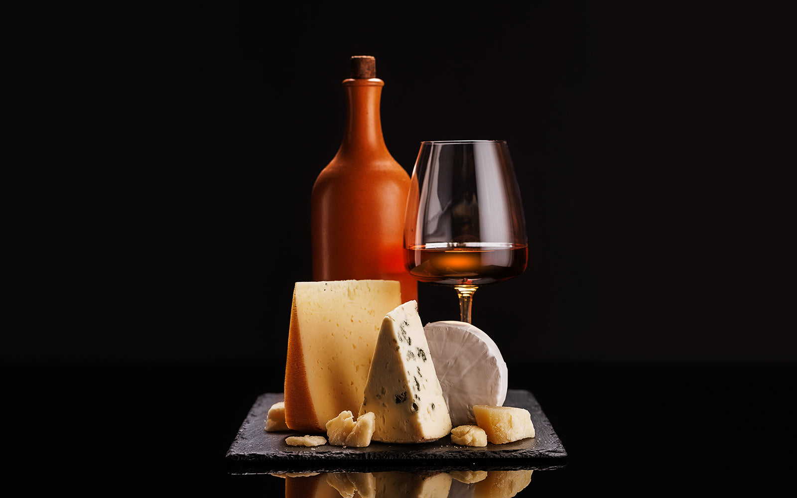 A bottle, an amber-filled glass and a board of cheeses including blue cheese, styled for a collector's pairing. Baroque Whisky Australian Single Malt.
