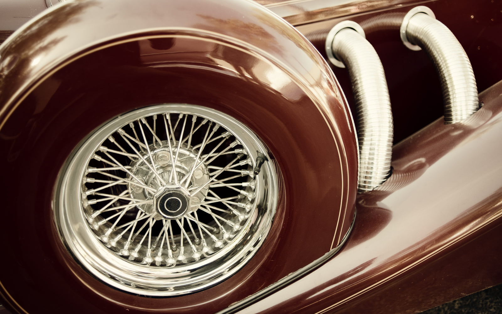 Close up of a vintage sports car wire wheel and exhaust, an analogue object that rewards the same patience as single cask whisky. Baroque Whisky Australian Single Malt.