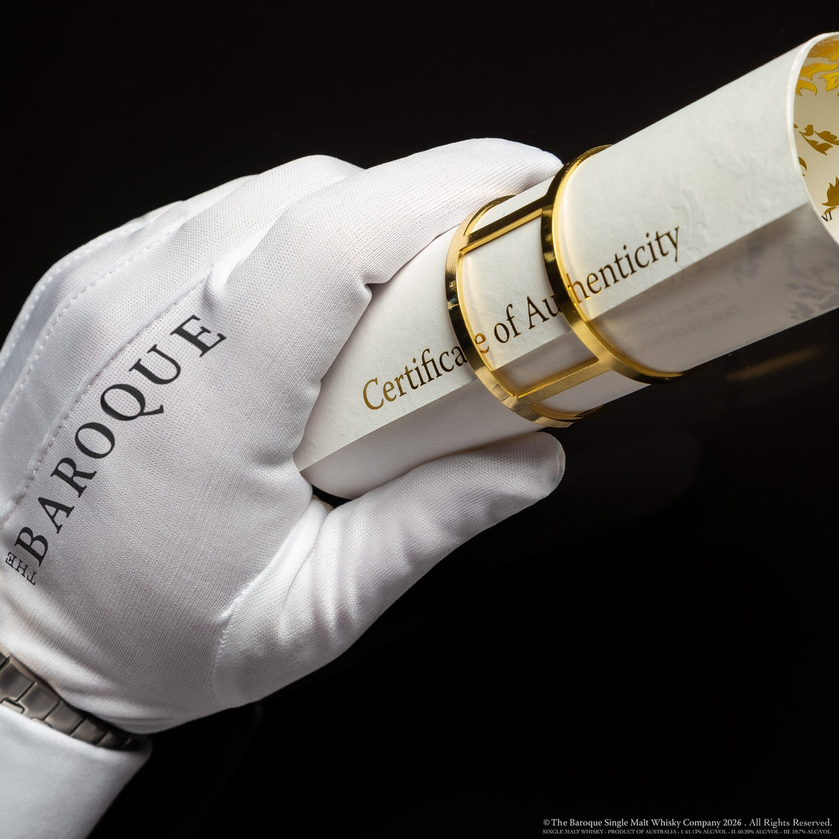 White gloved hand holding the rolled Baroque Whisky Certificate of Authenticity with its gold band, on black